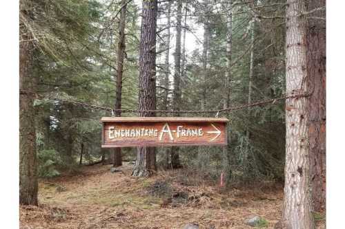 Wooden sign reading "Enchanting A-Frame" with an arrow, surrounded by tall trees in a forest.