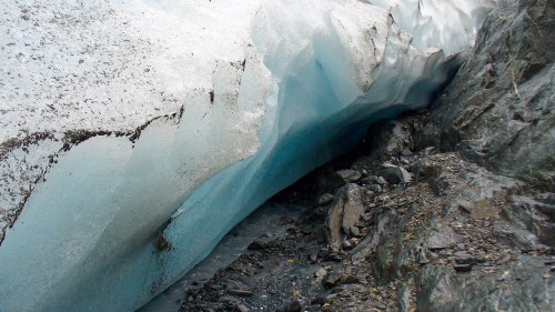 A close-up of a glacier with blue ice and rocky terrain, showcasing the texture and colors of the ice formation.