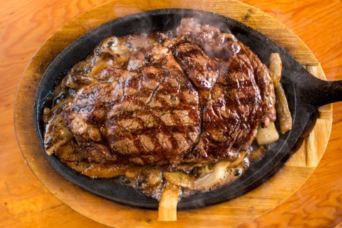 A sizzling steak on a hot skillet, surrounded by grilled onions, with steam rising in a warm, inviting setting.