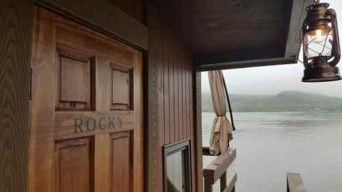 A wooden door labeled "ROCKY" next to a lantern, with a misty lake and hills in the background.
