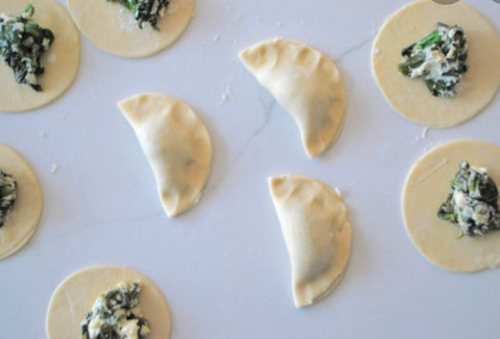Dough circles filled with spinach and cheese, some folded into half-moon shapes on a marble surface.