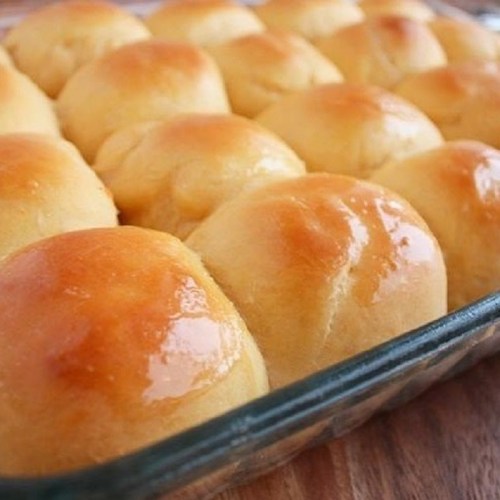 A close-up of golden-brown dinner rolls arranged in a glass baking dish, glistening with a buttery glaze.