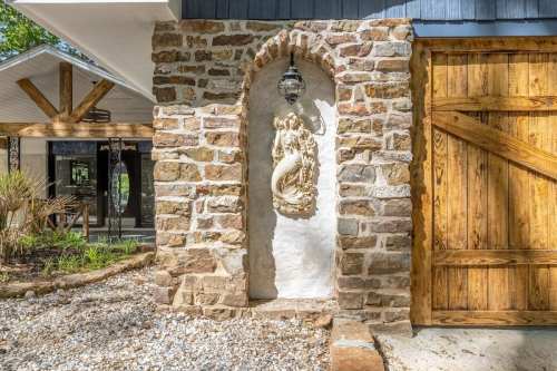 A stone wall with a decorative sculpture and lantern, next to a wooden door in a landscaped outdoor area.