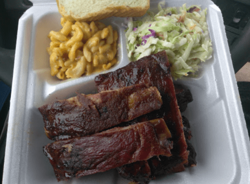 A takeout container with ribs, macaroni and cheese, coleslaw, and a slice of bread.