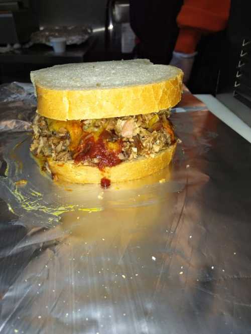 A stacked sandwich with shredded meat and sauce between two slices of bread, resting on aluminum foil.