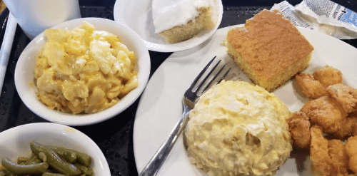 A plate with macaroni and cheese, chicken, green beans, cornbread, and dessert on a tray.