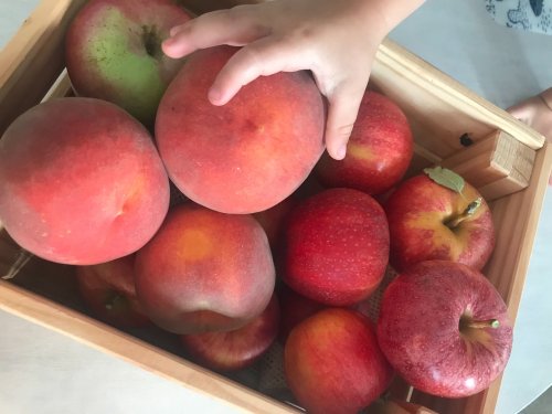 A hand reaching for a large peach among a basket of red apples and green fruit.