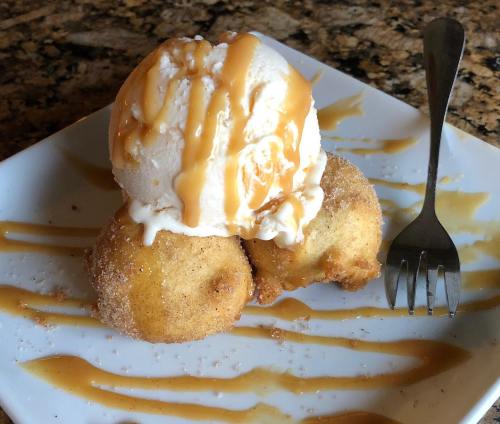 A plate with two fried dough balls topped with vanilla ice cream and drizzled with caramel sauce, alongside a fork.