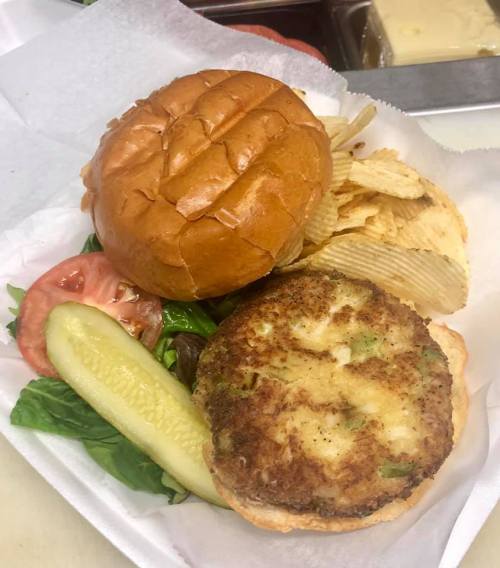 A sandwich with a crispy patty, lettuce, tomato, and pickles, served with potato chips on the side.