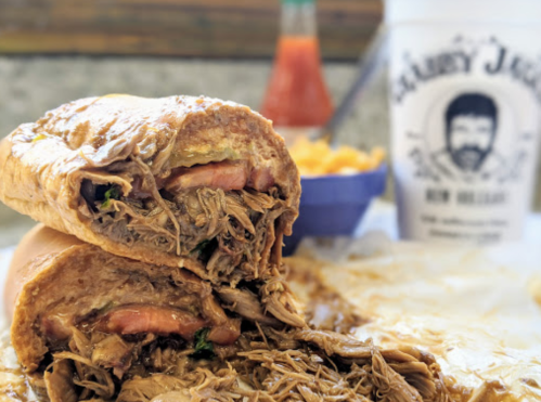 A close-up of a pulled pork sandwich, cut in half, with a side of macaroni and a drink in the background.