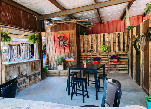 A rustic indoor space with wooden walls, a table, chairs, and decorative plants, creating a cozy atmosphere.
