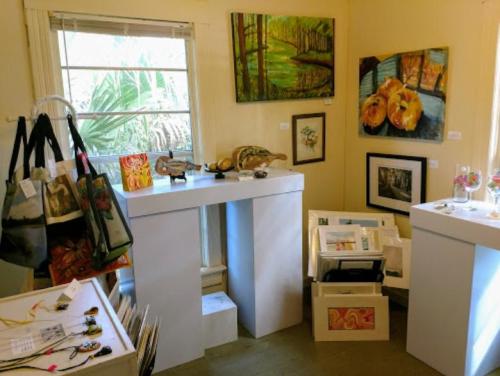 Art gallery interior featuring various artworks, display tables, and decorative items in a bright, inviting space.