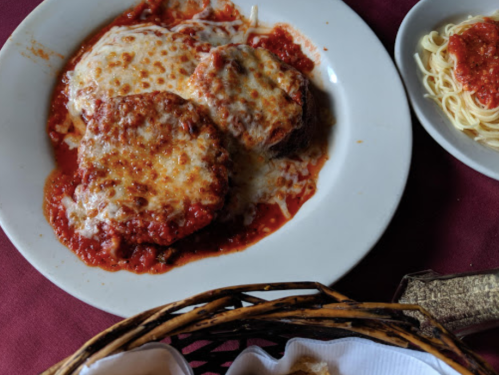 A plate of cheesy eggplant parmesan in marinara sauce, served with a side of spaghetti.