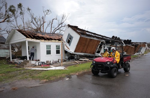 A damaged house with a collapsed roof and a utility vehicle nearby, as responders assess the storm's impact.