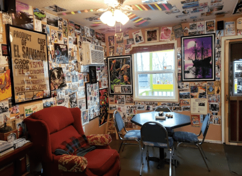 A cozy room with a red chair, a round table, and walls covered in various posters and photographs.