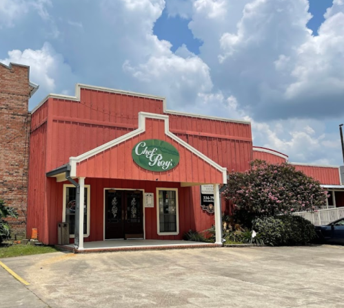 A red building with a sign reading "Chef Roy's," surrounded by greenery and under a partly cloudy sky.