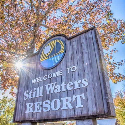 Sign for Still Waters Resort, surrounded by trees with autumn leaves and sunlight shining through.