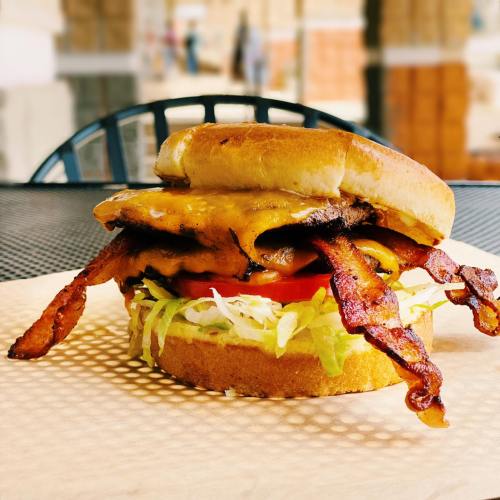 A delicious burger with melted cheese, lettuce, tomato, and crispy bacon on a toasted bun, served on a plate.