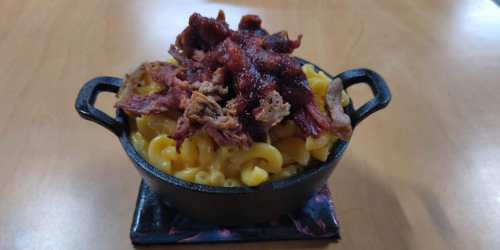 A cast iron dish filled with macaroni and cheese, topped with crispy, shredded meat.