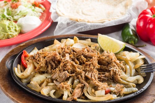 Sizzling fajitas with shredded meat, onions, and peppers, served with tortillas and fresh toppings on the side.