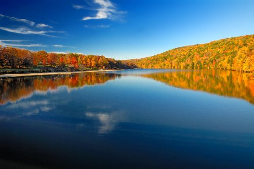 A serene lake surrounded by vibrant autumn foliage under a clear blue sky, reflecting the colorful trees.