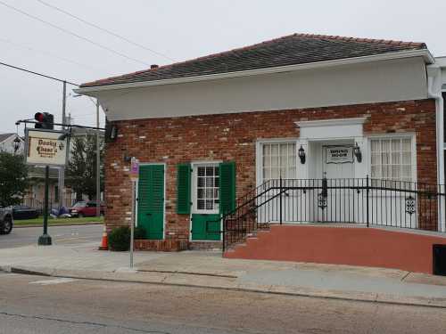 A brick building with green shutters and a ramp, next to a street with a sign for a nearby establishment.