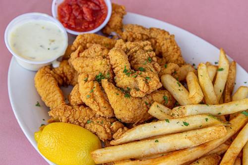 A plate of crispy fried chicken tenders, golden fries, a lemon wedge, and dipping sauces on a pink background.