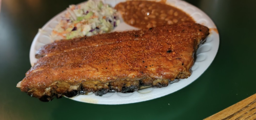 A plate featuring a large piece of grilled ribs, coleslaw, and baked beans.