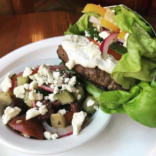 A lettuce-wrapped burger with toppings and a side salad featuring feta cheese and mixed vegetables.