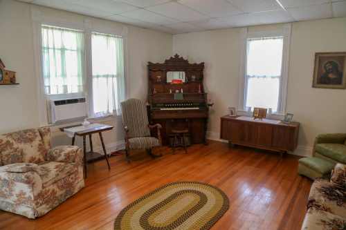 Cozy living room with vintage furniture, an organ, and large windows letting in natural light.