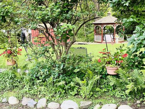 A lush garden scene featuring a gazebo, a shed, and hanging flower pots surrounded by greenery.