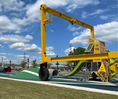 A colorful playground structure with a large yellow frame, slides, and climbing areas under a blue sky with clouds.