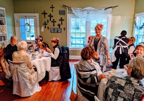 A group of women in elegant attire enjoying a gathering around tables in a warmly lit room with decorative crosses.