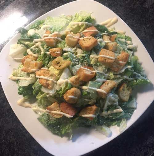 A fresh Caesar salad with romaine lettuce, croutons, and creamy dressing on a white plate.