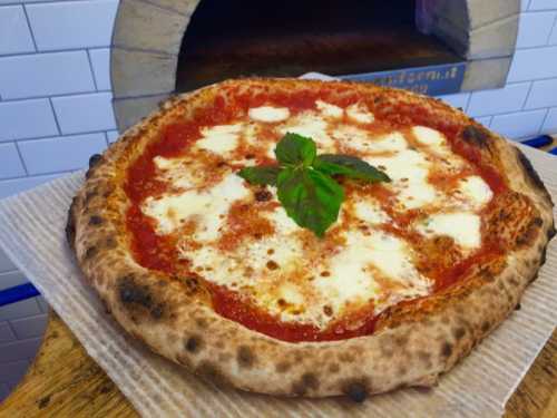 A freshly baked pizza with tomato sauce, mozzarella cheese, and a basil leaf, resting on a wooden surface.