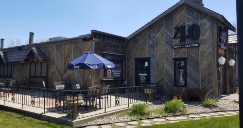 Exterior of a restaurant named "210 Steak & Seafood," featuring a patio with tables and an umbrella.
