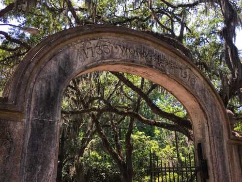 Archway with the inscription "1735 Worn 1913," surrounded by lush trees and Spanish moss.