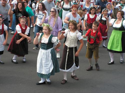 A group of people in traditional costumes dancing at a festival, with children in the foreground wearing flower crowns.