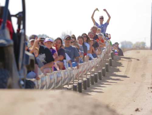 A long line of people enjoying a ride on a trailer, with one person playfully flexing their muscles in the background.