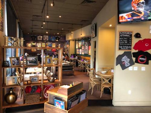 A cozy café interior with wooden furniture, wall art, and a TV showing a sports game. A display shelf is in the foreground.