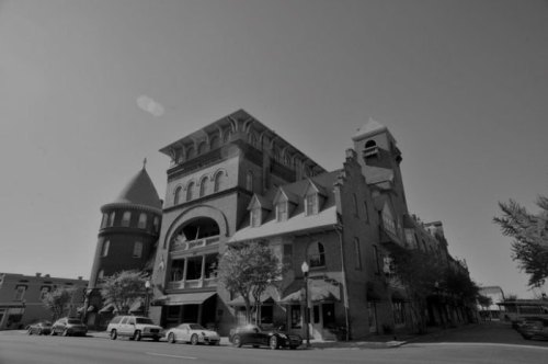 Historic building with a tower and ornate architecture, captured in black and white. Trees and cars are visible in the foreground.