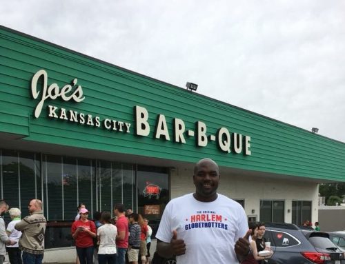 A person in a Harlem Globetrotters shirt poses outside Joe's Kansas City Bar-B-Que, with a crowd in the background.