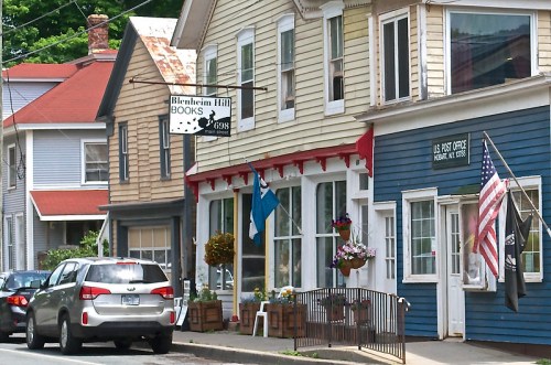 A quaint street scene featuring colorful buildings, a bookstore sign, and an American flag outside a post office.
