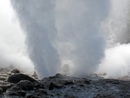 Steam erupts from geothermal vents, creating a dramatic display of vapor against a rocky landscape.