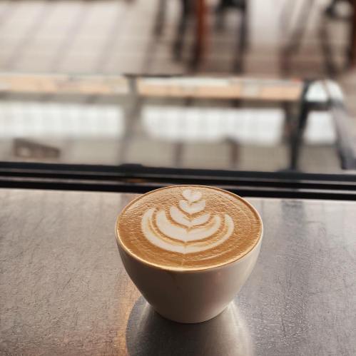 A latte in a white bowl with a beautiful leaf design on the surface, placed on a table in a café.