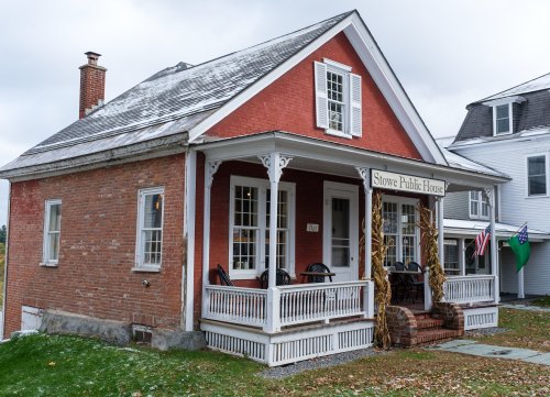 A red brick house with a porch, labeled "Stowe Public House," surrounded by autumn scenery and neighboring buildings.