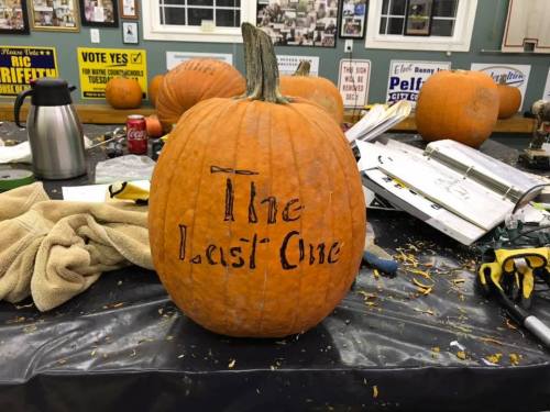 A carved pumpkin with the words "The Last One" displayed on a table surrounded by tools and other pumpkins.