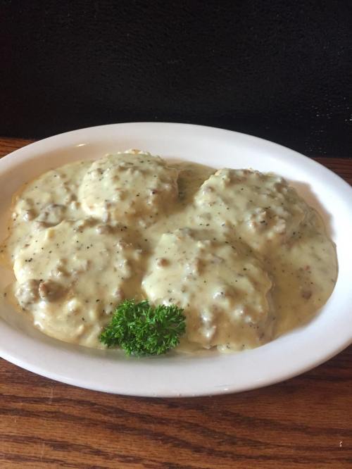 A plate of biscuits smothered in creamy sausage gravy, garnished with a sprig of parsley.