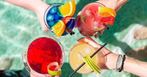 Four colorful cocktails with fruit garnishes held above a pool, reflecting a vibrant summer vibe.