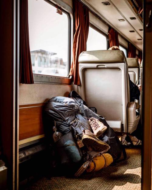 A travel backpack and boots rest against a train seat, with sunlight streaming through the windows.